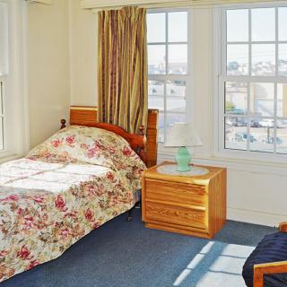 A cozy bedroom with a single bed, floral bedding, and a nightstand by large windows.
