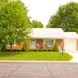 A suburban house with a well-maintained lawn and driveway, surrounded by trees.