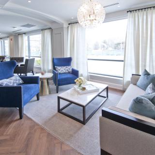 A modern living room featuring elegant blue chairs, a sleek coffee table, and bright lighting from a chandelier.