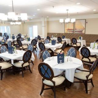An elegantly set dining room with round tables and upholstered chairs, ready for guests.