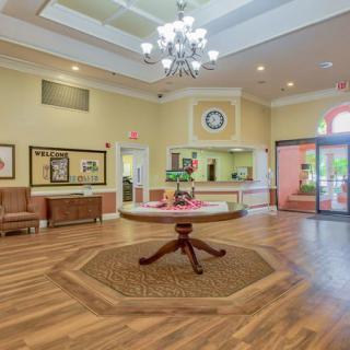 A well-lit hotel lobby with a chandelier, featuring a central decorative table and wooden flooring.