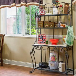 A kitchen corner with a decorative metal shelf unit, filled with various kitchen items and bathed in natural light from a nearby window.