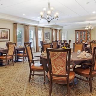 A spacious and elegantly decorated dining room with multiple round tables and ornate chairs, featuring chandeliers.