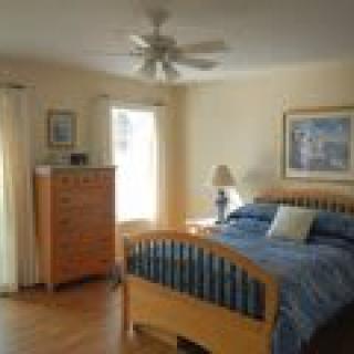 A cozy bedroom with a wooden bed and matching dresser, featuring a ceiling fan and large windows.