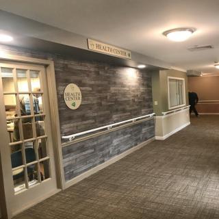 A well-lit hallway with a wooden door, handrails, and signage on the wall.