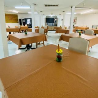 An empty dining hall with tables covered in brown tablecloths and a small centerpiece on each table.