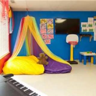 A colorful children's playroom with a rainbow canopy, comfortable beanbags, educational posters, and various activities.