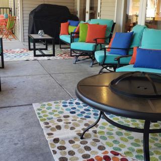 A cozy patio setup with colorful cushions, a fire pit, and a grill.