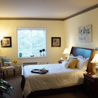 A cozy bedroom with a large window, decorated with elegant lamps and artwork.