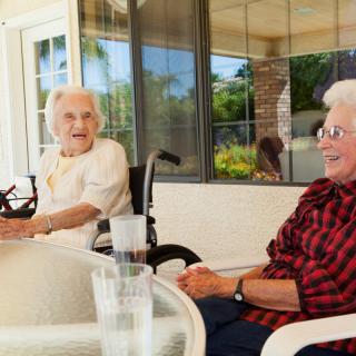 Two elderly women enjoying a conversation on a sunny patio.