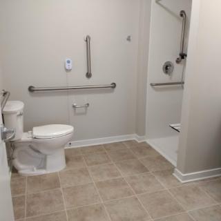 An accessible bathroom featuring grab bars, a toilet, and a walk-in shower.