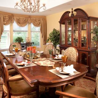 An elegantly furnished dining room with a large wooden table set for a meal, surrounded by ornate chairs and illuminated by a chandelier.