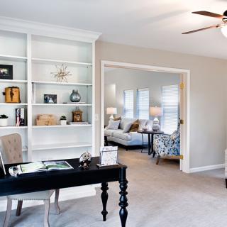 A stylish home office with a black desk and white bookshelves, opening into a bright and cozy living room.