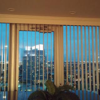 A view of a city skyline at dusk, framed by vertical blinds.