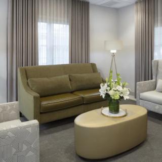 A modern living room with a green sofa, armchairs, and a coffee table adorned with flowers.