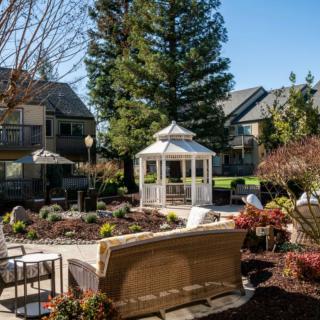 A serene outdoor garden with a white gazebo surrounded by patio furniture and landscaping.