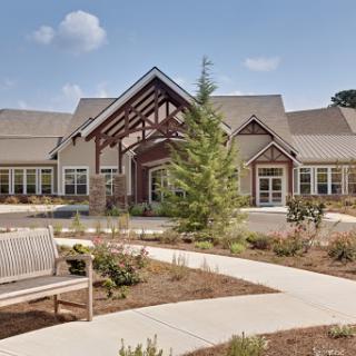 A modern residential building surrounded by landscaped grounds, featuring a welcoming entrance and seating area.