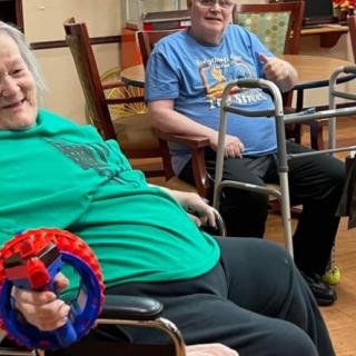Two elderly individuals enjoying a playful moment indoors, equipped with mobility aids and toys.