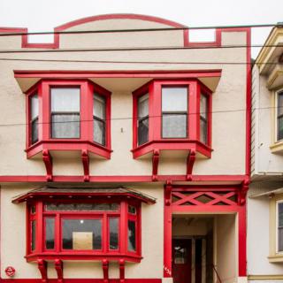 A two-story residential building with prominent red-trimmed bay windows.