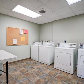 A clean laundry room featuring several washing machines and dryers, with a bulletin board on the wall.