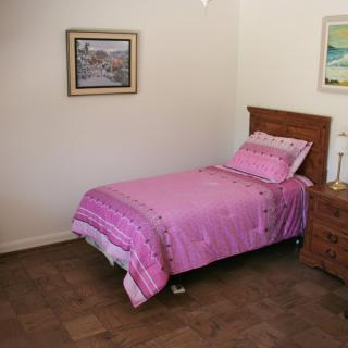 A simple bedroom with a single bed and pink bedding, featuring decorative paintings on the walls.