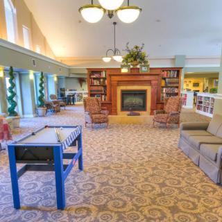 A cozy living room interior featuring a fireplace, comfortable seating, and bookshelves under warm lighting.