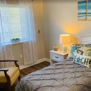 A cozy bedroom with a neatly made bed, soft lighting from a lamp, and a chair by the window.