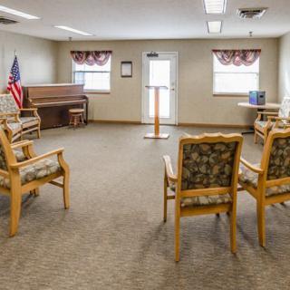 A small meeting room with chairs arranged in a circle, featuring a podium, piano, and an American flag.