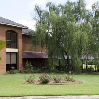 A modern brick building surrounded by trees and a well-maintained lawn.
