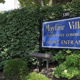 Entrance sign for Mayfair Village Apartment Community surrounded by lush greenery.