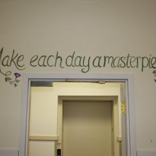 A motivational quote on the wall reads 'Make each day a masterpiece,' set above a door frame.