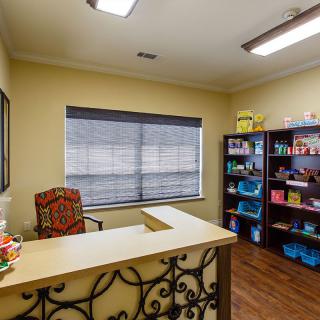 A tidy office reception area with a desk, chair, and shelves in a well-lit room.