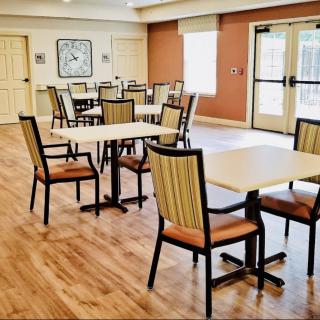 An empty dining room with neatly arranged tables and chairs on a wooden floor, well-lit by natural sunlight.