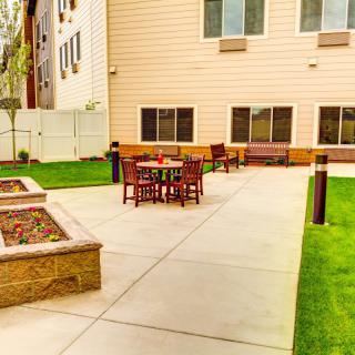 A well-maintained patio area with tables and chairs, surrounded by grass and bordered by a building.
