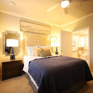 A cozy bedroom with a neatly made bed, flanked by nightstands and lamps, featuring warm lighting and elegant decor.
