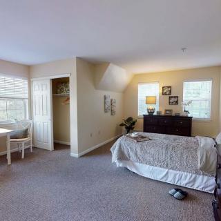 A spacious bedroom with a neatly made bed, dresser, and natural light streaming through large windows.