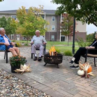 Three people sitting around a fire pit with autumn decorations.