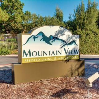 An entrance sign for Mountain View, featuring a mountain graphic and surrounded by greenery.