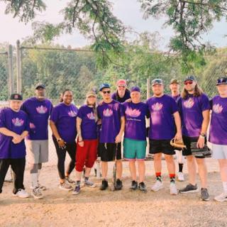 A spirited group of friends gathered for a fun day of softball in vibrant purple team shirts.