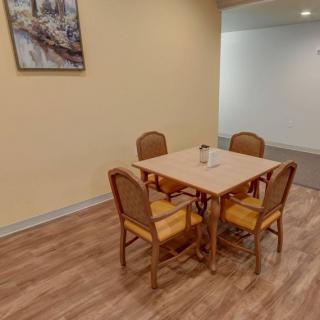 A cozy dining area with a wooden table and four chairs, set against a warm-toned wall adorned with a painting.