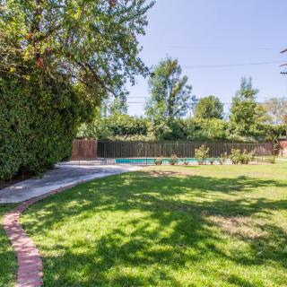 A spacious backyard featuring a well-maintained lawn, surrounded by trees and a wooden fence, with a stone pathway leading through the garden.