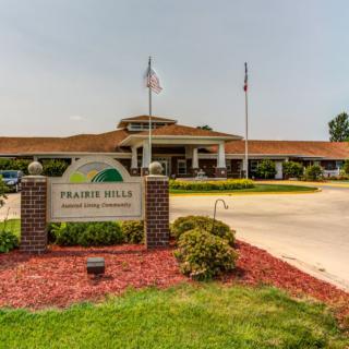 Entrance to a building with a sign labeled 'Prairie Hills Assisted Living Center' and landscaped surroundings.
