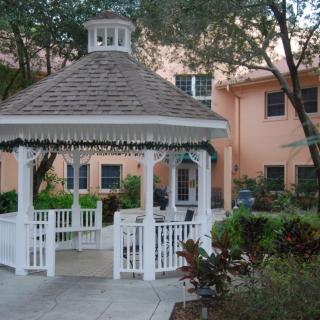 A picturesque white gazebo in a garden setting surrounded by greenery and trees.