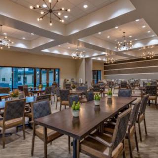 A spacious and modern dining hall with elegant chandeliers and neatly arranged tables and chairs.
