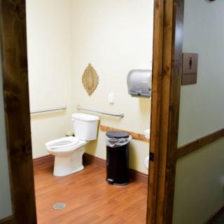 An accessible restroom with a toilet, trash can, and paper towel dispenser.