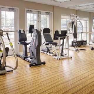 A well-lit gym room featuring various exercise equipment on a wooden floor.