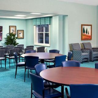 A well-lit seating area with round tables and blue chairs, featuring artwork on the walls and a large window.