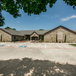 A stone building with a central entrance, set against a clear blue sky and framed by leafy trees.