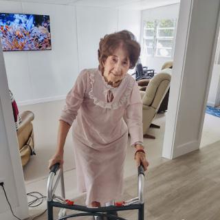 An elderly woman using a walker in a bright living room.