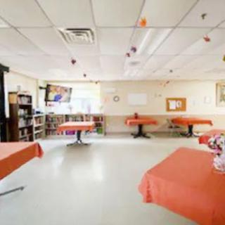 A classroom with tables covered in orange cloth, decorated ceiling, and shelves filled with books.